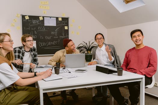 A diverse team of young professionals sharing ideas and laughing during a business meeting in a modern office setting.