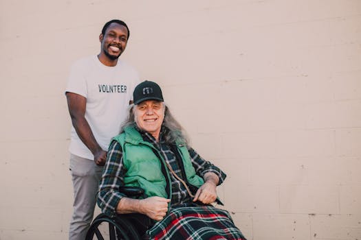 A volunteer helps a smiling man in a wheelchair outside, showcasing community support and kindness.