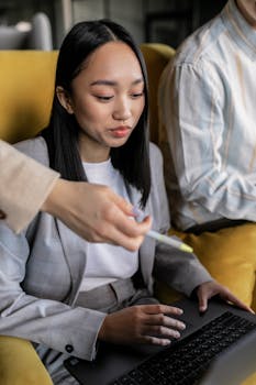 Asian woman in blazer focused on using laptop, representing technology and teamwork.