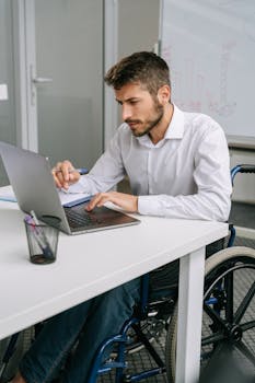 Man using a laptop at a desk in an office setting, highlighting accessibility and technology use.